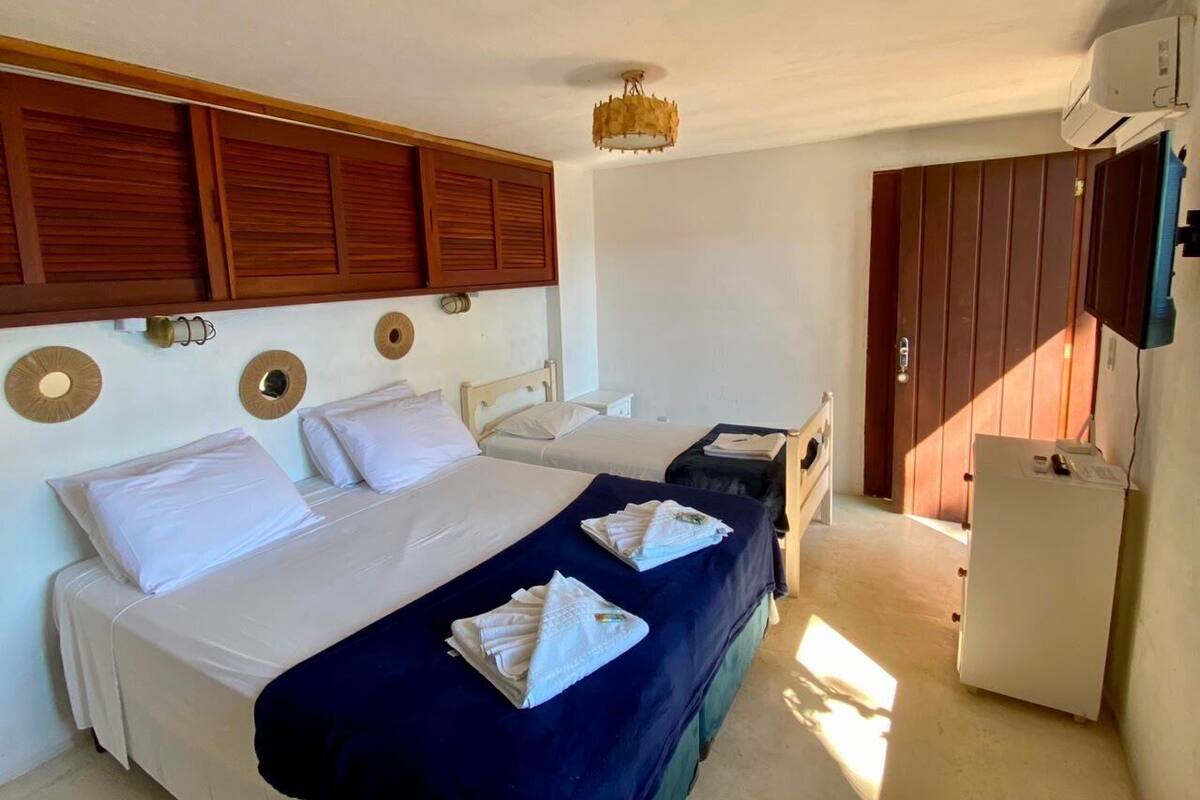 A hotel room with two beds, a small desk, a refrigerator, and a wardrobe.