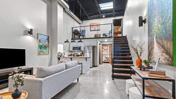 A modern interior with a sofa, a flat-screen TV, a staircase, and a dining area. - Lambeau Loft - Downtown GB & KI Convention (Green Bay)