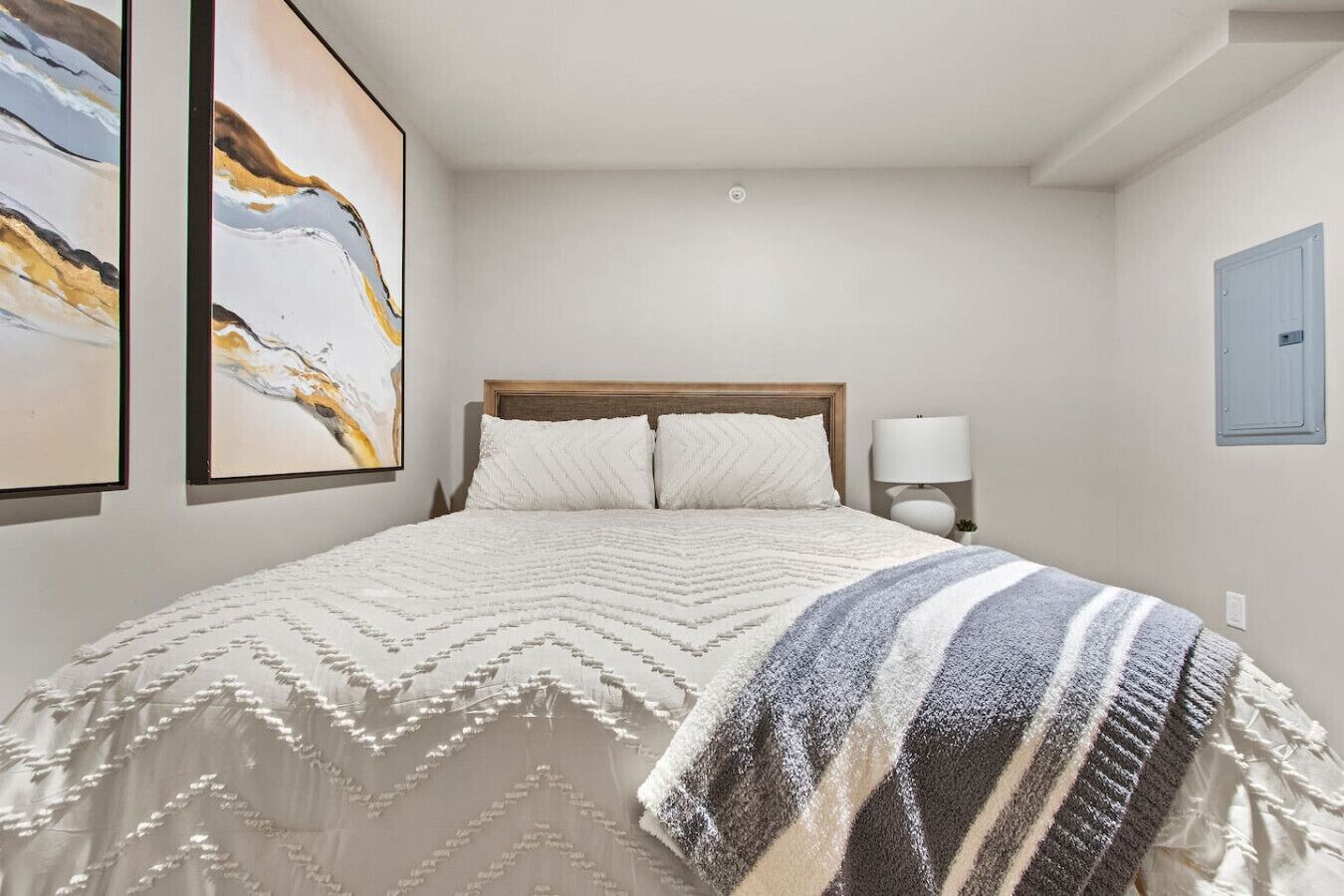 Ein Schlafzimmer mit einem Bett, zwei an der Wand befestigten Bildern, einer Nachttischlampe und einer blauen Tür.
