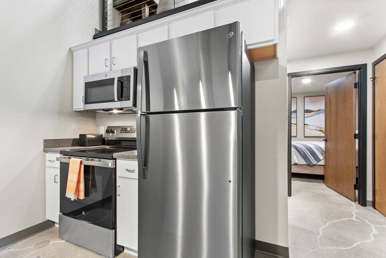 A compact kitchen with a stainless steel refrigerator, microwave, oven, and a small stovetop.