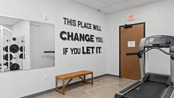 Un gimnasio con una frase motivacional en la pared, una cinta de correr y un banco.
