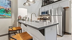 A modern kitchen with a granite countertop, stainless steel appliances, a bar stool, and pendant lighting. - Lambeau Loft - Downtown GB & KI Convention (Green Bay)