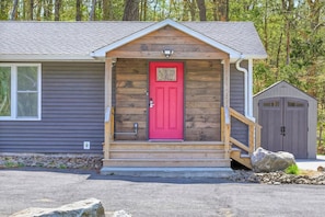 A small wooden cabin with a red door, a porch, and a garage.