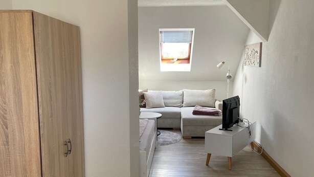 Quarto com guarda-roupa de madeira, sofá, mesa pequena, televisão e janela.