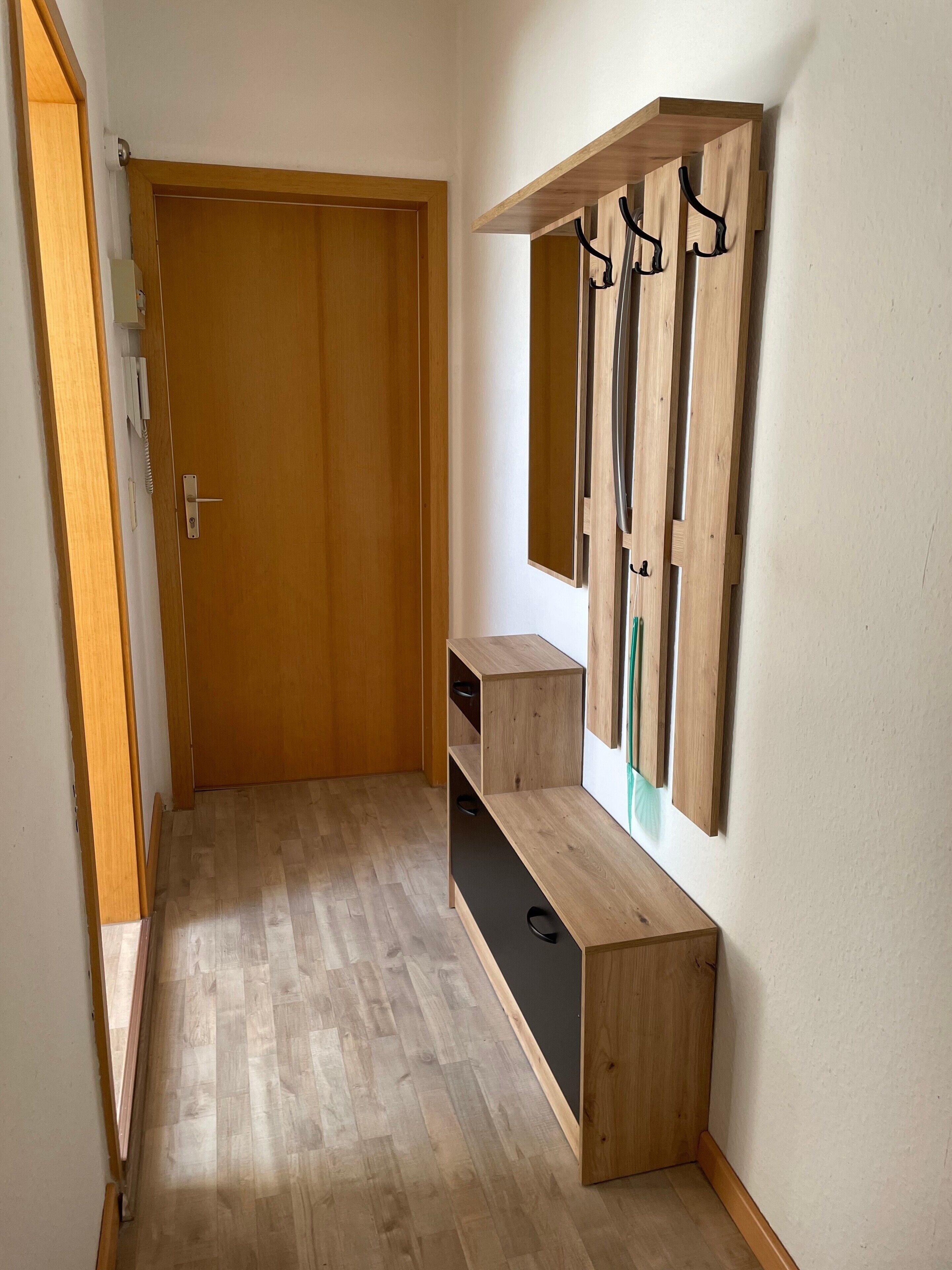 A hallway with a wooden door, a wooden bench with a mirror and hooks, and a small shelf.