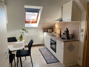 Eine kleine Küche mit Essecke, Heizkörper, Fenster mit Jalousien und einer Zimmerpflanze.