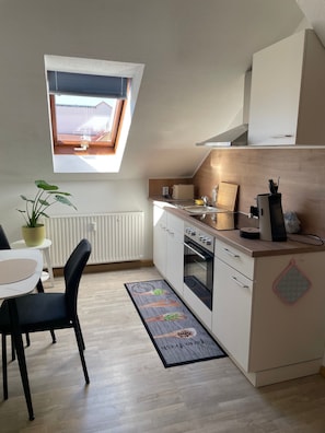 Une cuisine de taille réduite avec une fenêtre, un coin repas avec des chaises et un radiateur.