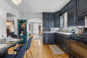 A modern kitchen with dark cabinets, a stove, and a dining area with a table and chairs. - AfterWIRTZ - Walking distance to Lambeau/Resch Ctr (Green Bay)
