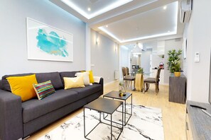 A modern living room with a grey sofa, a coffee table, and a dining area with chairs and a table. - Charming Modern Apartment in Central Madrid (Madrid)