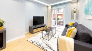 Een moderne woonkamer met een flatscreen televisie, een grijze bank, een salontafel en een groot raam.