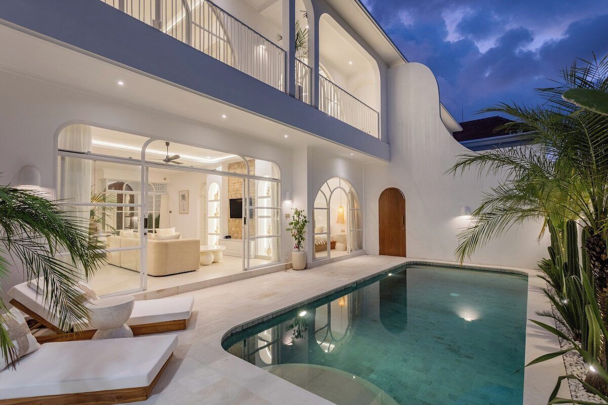 A modern house with a pool, a balcony, and a well-lit interior.