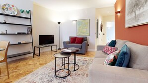 Een woonkamer met een bank, fauteuil, televisie, boekenkast en een schilderij aan de muur.