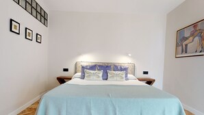 Een slaapkamer met een bed, nachtkastjes, een aan de muur bevestigde lamp en een lijst met een afbeelding.