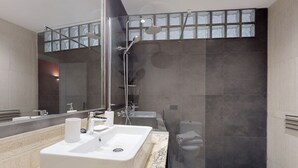 Een moderne badkamer met een grote spiegel, een badkuip, een douche en een toilet.
