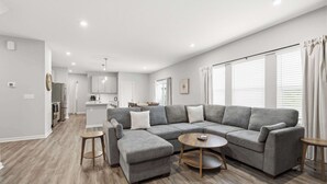 Una sala de estar moderna con un sofá seccional, una mesa de centro redonda y una cocina al fondo.