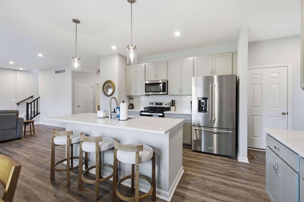 A modern kitchen with a central island, stainless steel appliances, and wooden bar stools.