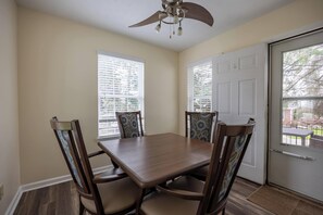 A dining area with a wooden table and four chairs, a ceiling fan, and a door with a window.