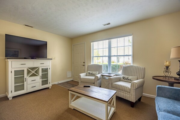 A living room with a TV, white furniture, a window, and a door.