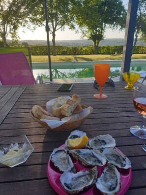 A table with a basket of bread, a plate of oysters, a glass of wine, and a glass of orange juice.