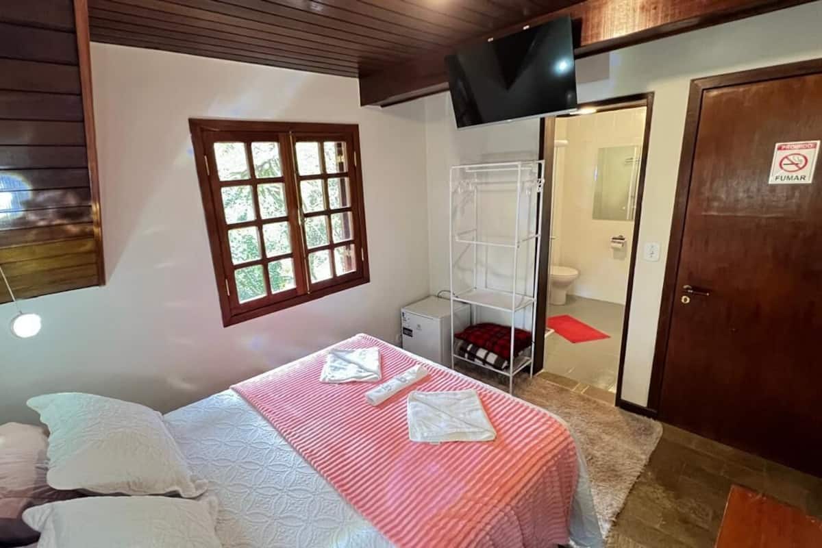 A bedroom with a bed, a window, a TV, a wardrobe, and a bathroom door.