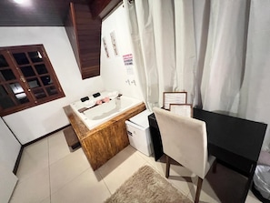 Une chambre avec une coiffeuse en bois, un petit réfrigérateur, une chaise, un bureau et une fenêtre avec des rideaux.