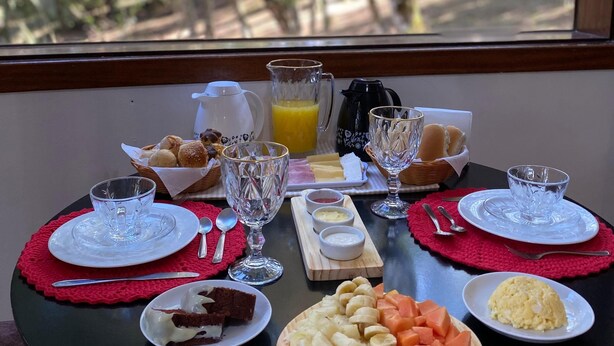 A breakfast table with a variety of food items, a pitcher of orange juice, and a view of a forest through a window. - villaggio farnese (Campos do Jordão)