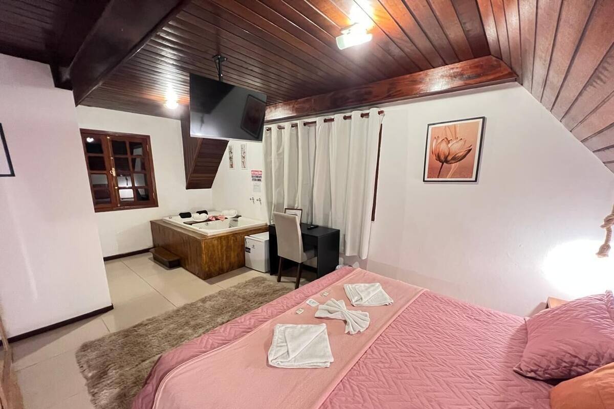 A bedroom with a bed, a desk, a chair, a small table, and a window.