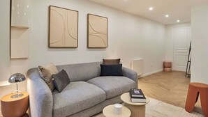 Un salon moderne avec un canapé gris, une petite table basse ronde, un lampadaire et des œuvres d’art abstraites accrochées au mur.