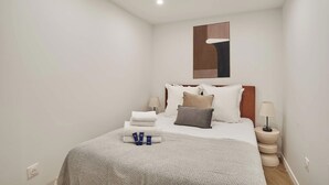 Une chambre d’hôtel bien rangée, avec un lit, des oreillers, une table de chevet avec une lampe et un luminaire fixé au mur.