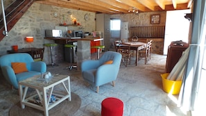 A rustic interior with stone walls, wooden beams, a dining area with a table and chairs, and a kitchenette with appliances.