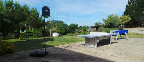A concrete outdoor area with a ping pong table, a basketball hoop, and a swing set.