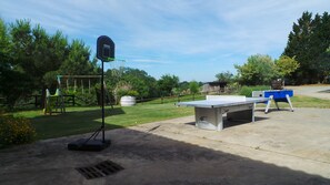 Un espacio exterior de concreto con mesa de ping pong, aro de baloncesto y columpio.