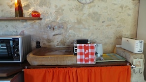 Una cocina con pared de piedra, encimera de madera, un lavabo, un tostador y un reloj.
