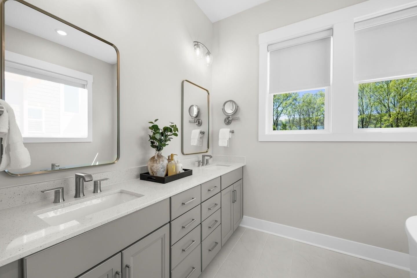 Un baño moderno con dos lavamanos, un espejo grande, una ventana con vistas a árboles y una planta pequeña en la encimera.