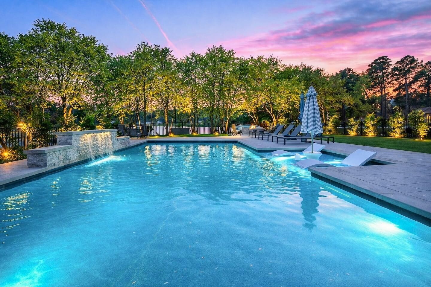 A swimming pool with a stone waterfall feature, surrounded by trees and lounge chairs.