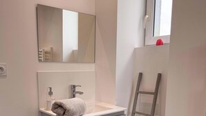 A bathroom with a white sink, a mirror, a towel, a bottle of liquid soap, and a wooden ladder. - Tranquiloue - Grand Gite Familial 10min Puy du Fou (Les Epesses)