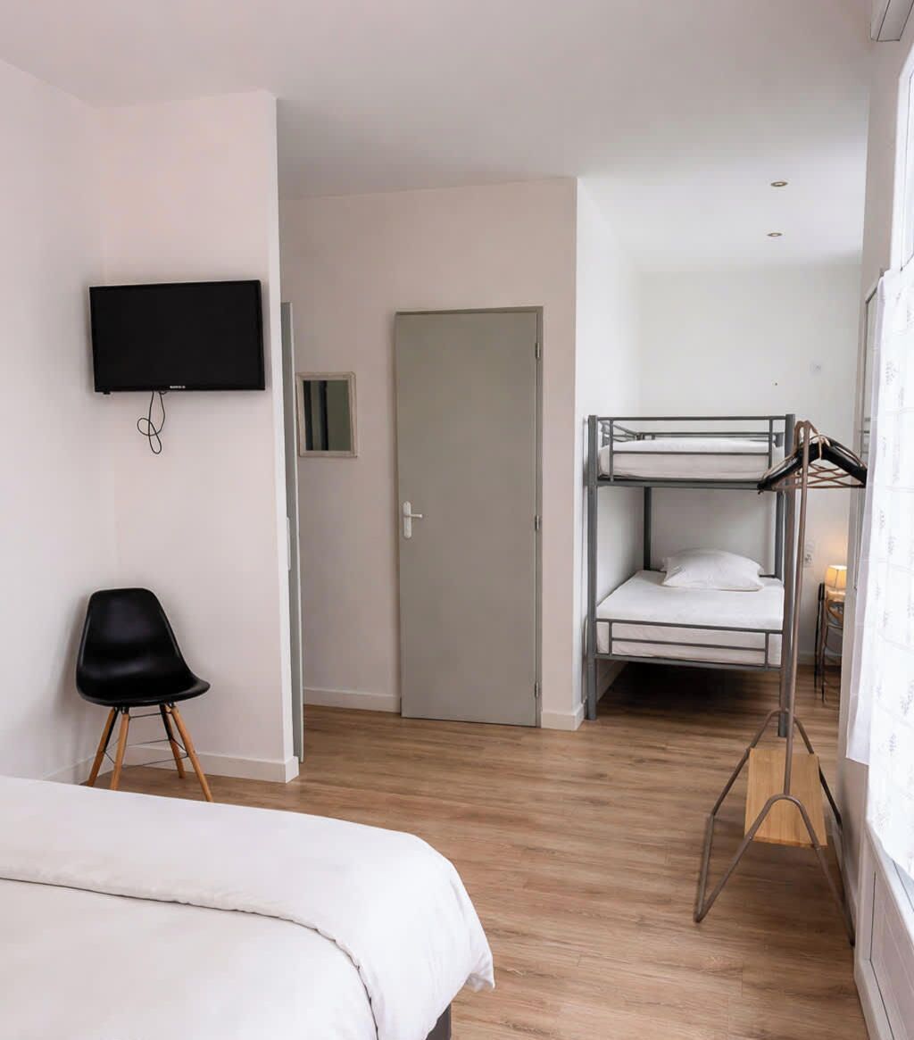 Une chambre avec un lit superposé, un lit simple, une chaise, un téléviseur et une porte.