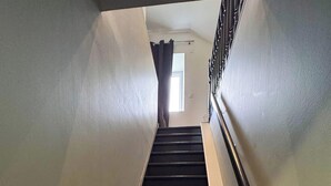 A staircase with a handrail, leading to a landing with a window and a door. - Tranquiloue - Grand Gite Familial 10min Puy du Fou (Les Epesses)