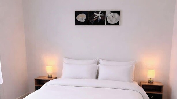 A neatly made bed with white bedding, two bedside tables with lamps, a small bench, and a wall-mounted artwork. - Tranquiloue - Grand Gite Familial 10min Puy du Fou (Les Epesses)