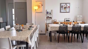 A modern dining area with a long table, white chairs, and a variety of tableware. - Tranquiloue - Grand Gite Familial 10min Puy du Fou (Les Epesses)