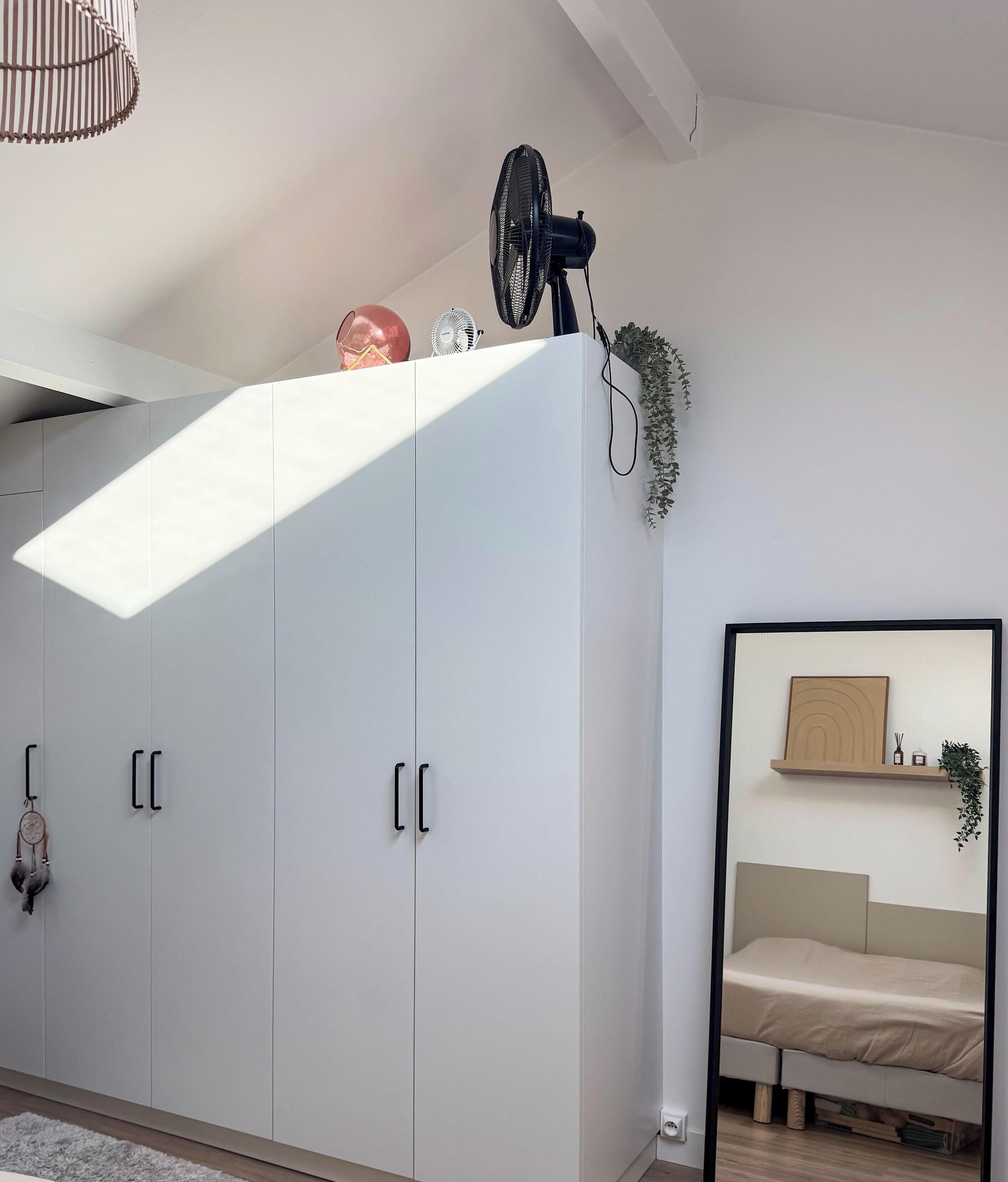 A bedroom with a bed, a white wardrobe, a ceiling fan, and a skylight.