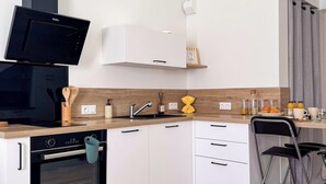 Una cocina moderna con armarios blancos, una campana extractora negra, un horno empotrado, un lavamanos y un comedor con una silla.