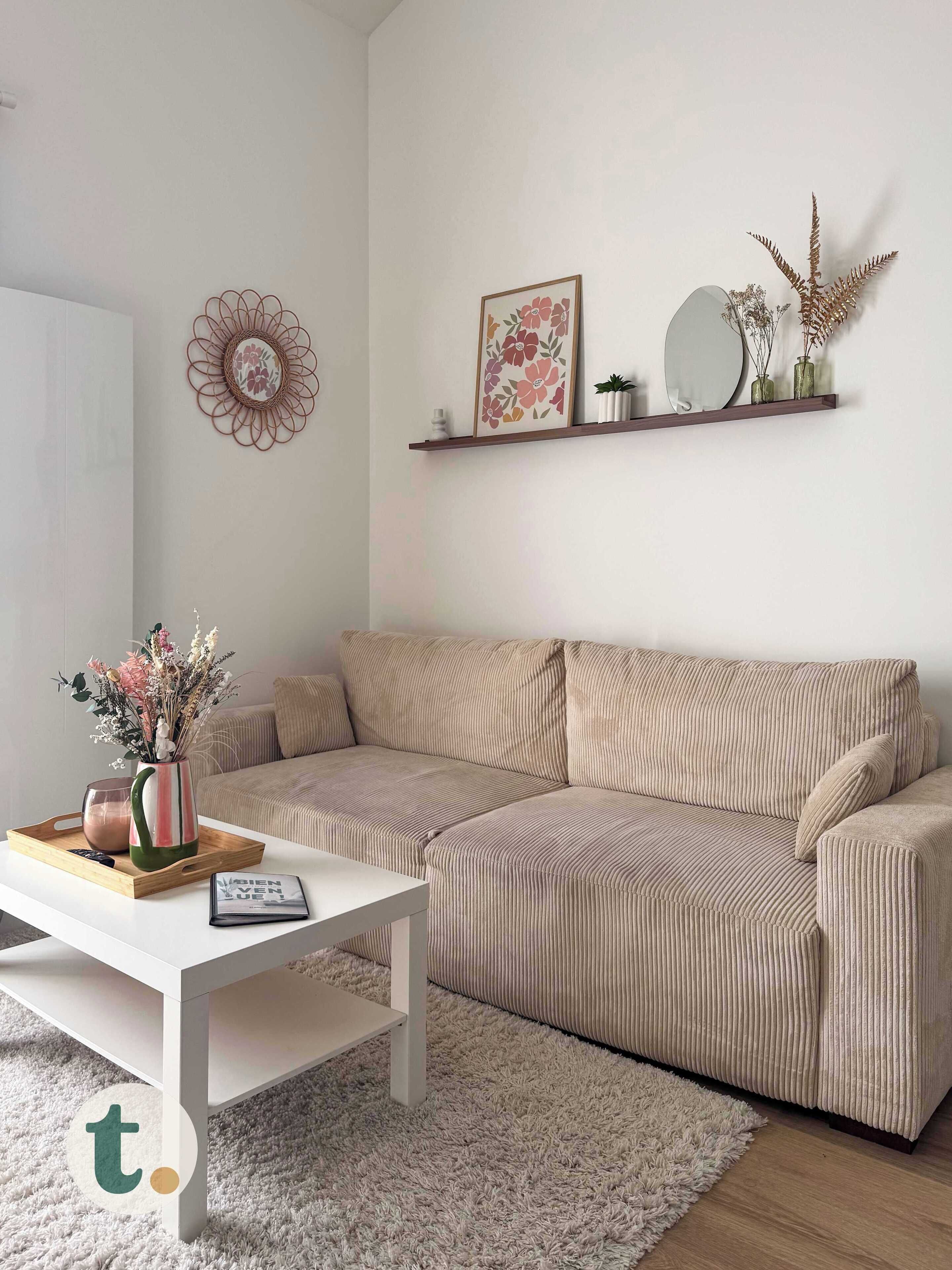 Un salon avec un canapé beige, une table basse blanche, un élément décoratif mural et une étagère avec des plantes.