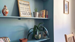 Ein Zimmer mit blauer Wand, einem Bücherregal mit Büchern und Dekorationsgegenständen, einem gerahmten Motivationszitat, einer Topfpflanze und einem gerahmten Bild an der Wand.