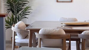 Un comedor con mesa de madera, sillas blancas acolchadas, una planta colgante y obras de arte botánicas enmarcadas en la pared.