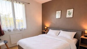 Un dormitorio con cama, mesitas de noche, ventana con cortinas y una obra de arte en la pared.