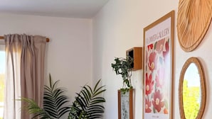 Una habitación con una planta en maceta, una galería de flores enmarcadas y un espejo en la pared.