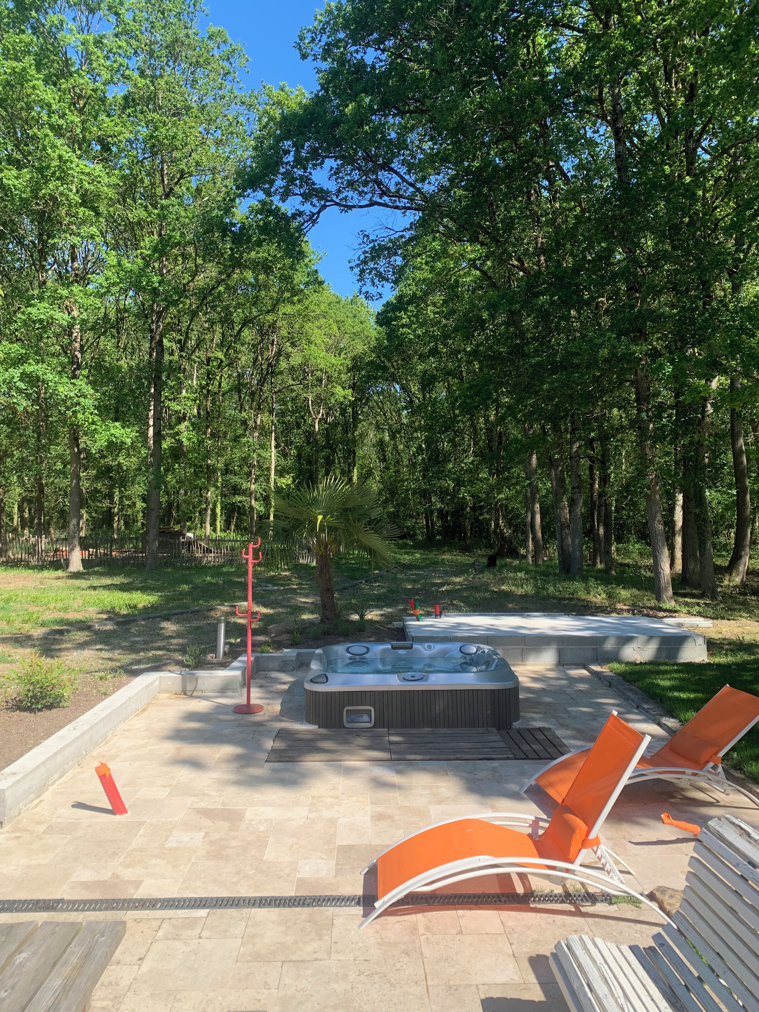 A hot tub surrounded by orange chairs, a wooden deck, and a forested area.