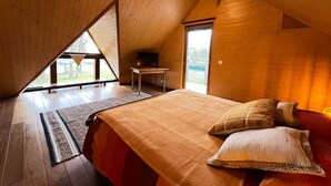 Un dormitorio con techo inclinado, una cama con almohadas, una mesita pequeña y una ventana.
