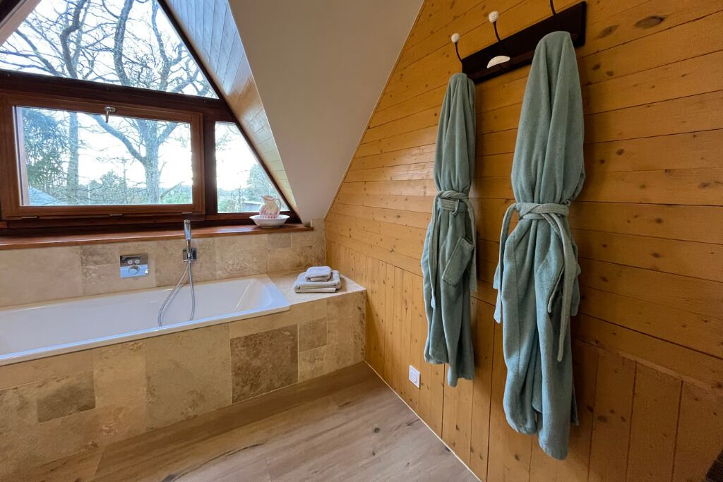 A bathroom with a bathtub, wooden walls, and a window.